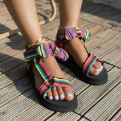 Sandali estivi colorati con suola nera, design a righe multicolore, indossati su piedi femminili con smalto bianco. Moda estiva, calzature trendy.