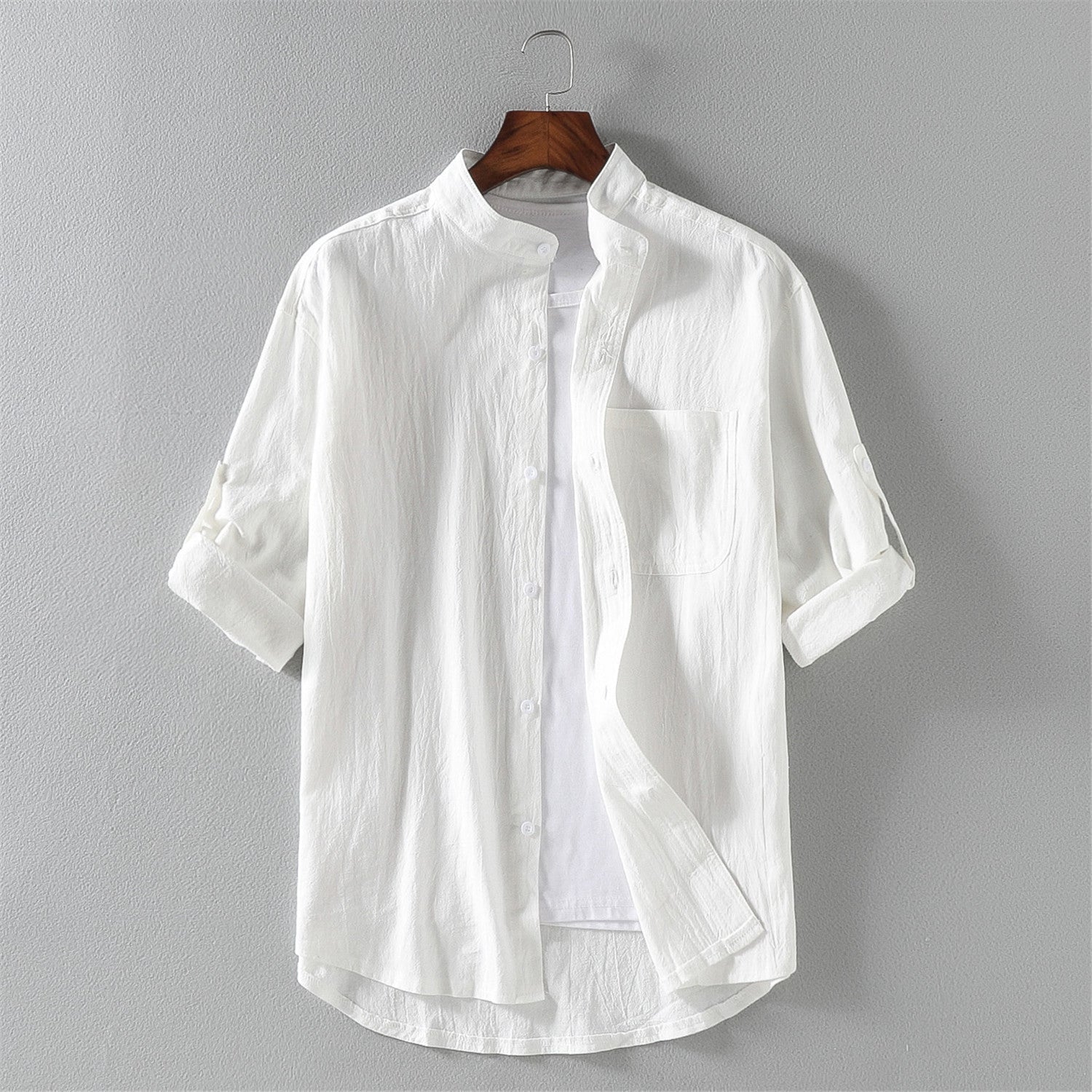 Camicia bianca da uomo in cotone, maniche lunghe arrotolate, colletto alla coreana, design casual elegante, appesa su gruccia.