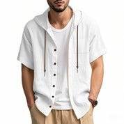 Camicia bianca da uomo con cappuccio, maniche corte, bottoni marroni, cordini, indossata sopra t-shirt bianca. Stile casual estivo.