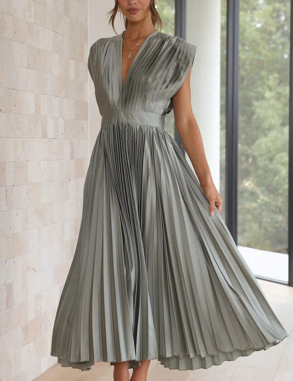 Abito lungo plissettato grigio elegante, senza maniche, indossato da una donna in interni moderni. Perfetto per eventi formali e cerimonie.