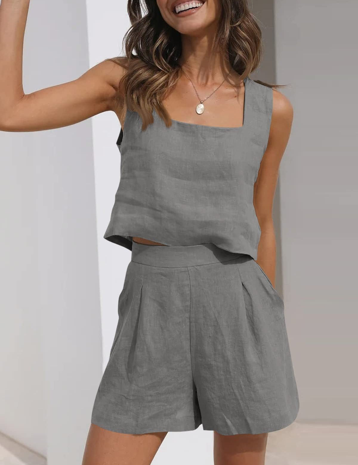Donna sorridente indossa completo estivo grigio in lino, top senza maniche e pantaloncini a vita alta. Moda casual elegante, abbigliamento estivo donna.