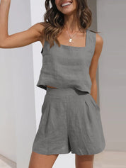 Donna sorridente indossa completo estivo grigio in lino, top senza maniche e pantaloncini a vita alta. Moda casual elegante, abbigliamento estivo donna.