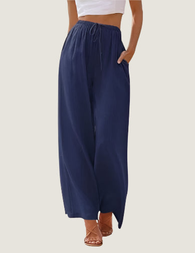 Pantaloni palazzo blu scuro da donna, vita alta con coulisse, tasche laterali, abbinati a top bianco e sandali marroni.