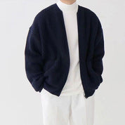 Giacca cardigan blu scuro a coste, indossata su maglione bianco e pantaloni bianchi. Moda uomo casual, abbigliamento autunnale elegante.