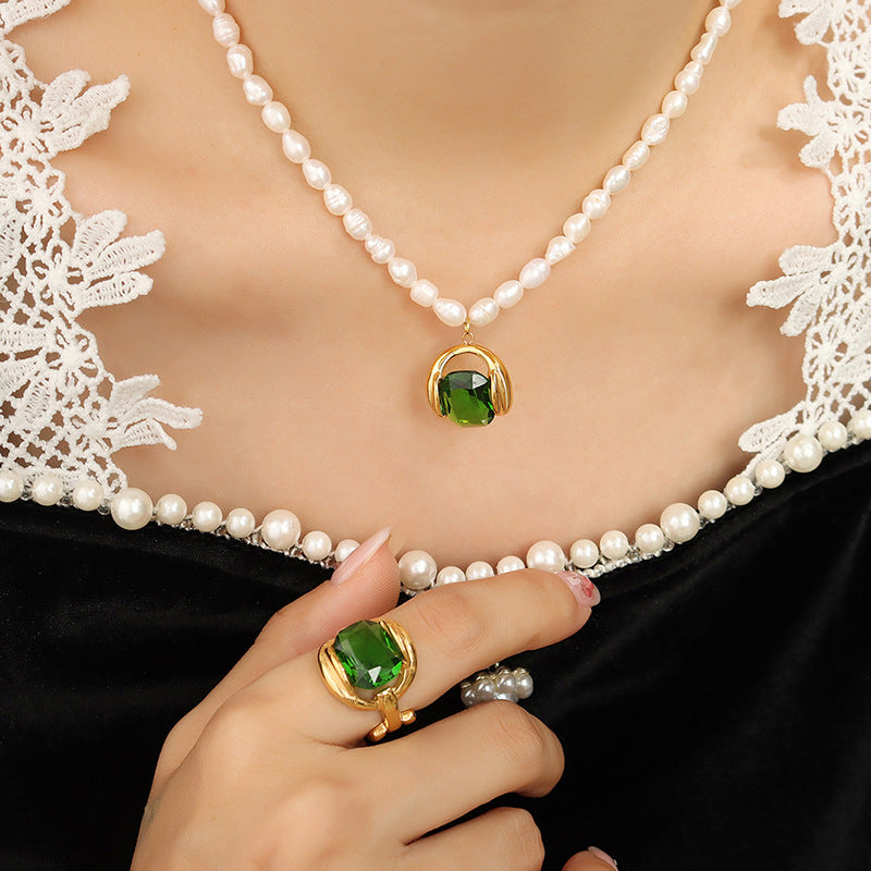 Collana di perle con ciondolo verde e anello coordinato su sfondo di pizzo bianco. Gioielli eleganti, moda donna, accessori di lusso.