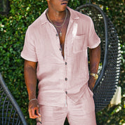 Uomo in abito estivo rosa chiaro, camicia a maniche corte e pantaloni coordinati, sfondo verde. Moda maschile casual, look estivo elegante.