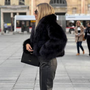 Donna con cappotto di pelliccia nera, occhiali da sole e borsa elegante in una piazza urbana. Moda invernale, stile chic, abbigliamento di lusso.