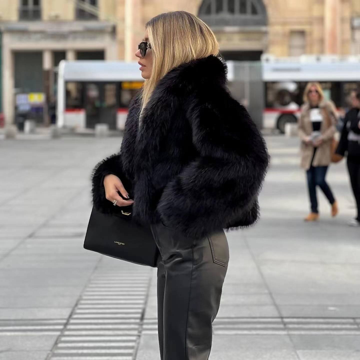 Donna con cappotto di pelliccia nera, occhiali da sole e borsa elegante in una piazza urbana. Moda invernale, stile chic, abbigliamento di lusso.