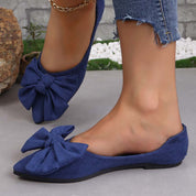 Scarpe ballerine blu con fiocco grande, indossate su pavimento grigio. Moda donna, calzature eleganti, stile casual, jeans strappati.