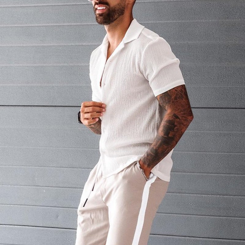 Uomo con camicia bianca a maniche corte e pantaloni beige, posa casual. Moda estiva maschile, abbigliamento elegante e moderno.