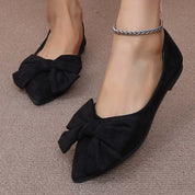 Scarpe ballerine nere da donna con fiocco, indossate su tappeto beige. Eleganti e comode, ideali per moda casual e formale.
