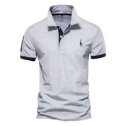Polo uomo grigia, maniche corte, colletto classico, logo ricamato, dettagli blu scuro. Elegante e casual, ideale per moda maschile estiva.