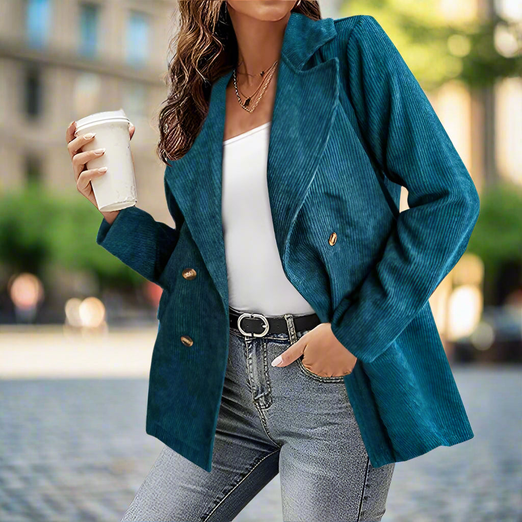 Donna con giacca blu a coste, top bianco e jeans, tiene una tazza da caffè. Moda urbana, abbigliamento casual chic, stile autunnale.
