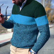 Maglione uomo a righe blu e verde, lavorato a maglia, indossato con pantaloni beige. Stile casual autunnale, moda maschile elegante.