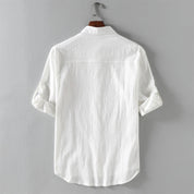 Camicia bianca da uomo in cotone, maniche lunghe arrotolate, appesa su gruccia. Design classico, ideale per look casual ed eleganti.