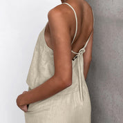 Donna in abito estivo beige con spalline sottili e schiena scoperta, tessuto leggero, moda casual elegante, perfetto per giornate calde.