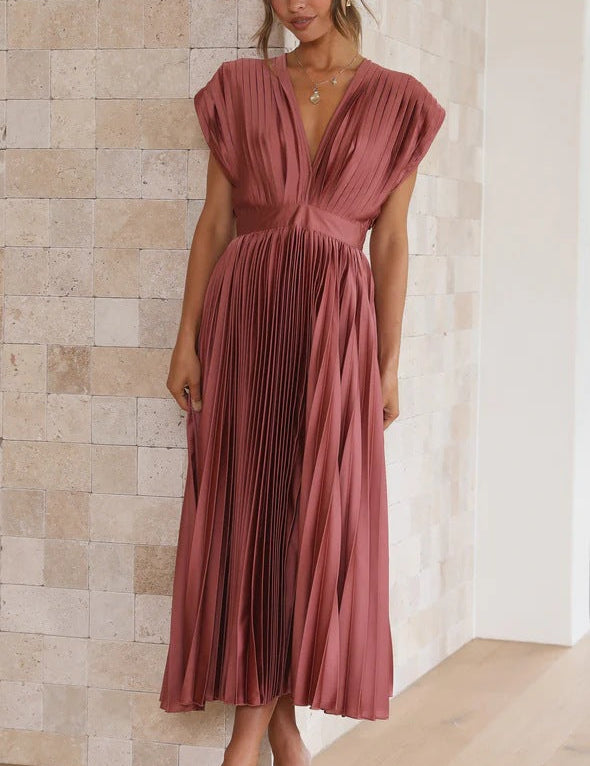 Abito lungo plissettato rosa antico, scollo a V profondo, maniche corte, indossato da donna in sandali beige. Elegante moda femminile estiva.