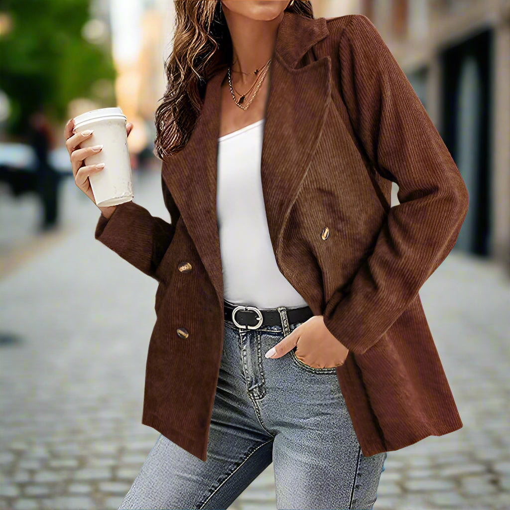 Giacca marrone a coste su donna con caffè in mano, jeans e cintura nera. Moda autunnale casual in strada urbana.