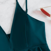 Abito verde smeraldo con spalline sottili su sfondo bianco, elegante e moderno. Occhiali da sole rossi a lato. Moda donna, abbigliamento estivo.