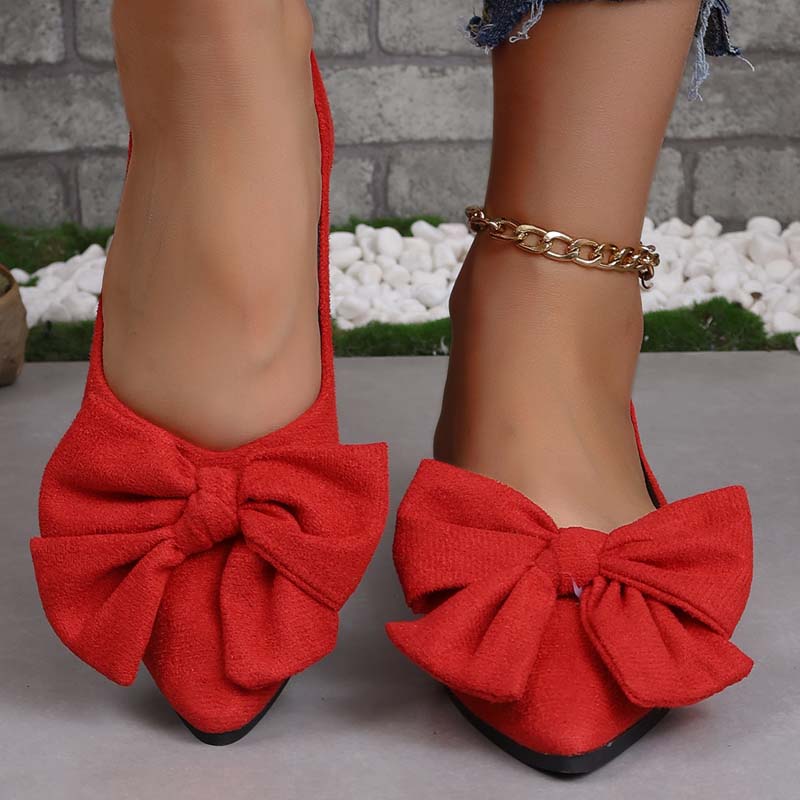 Scarpe ballerine rosse con fiocco grande, indossate su pavimento grigio. Accessorio cavigliera dorata. Scarpe eleganti da donna, moda casual.