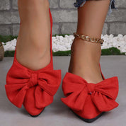Scarpe ballerine rosse con fiocco grande, indossate su pavimento grigio. Accessorio cavigliera dorata. Scarpe eleganti da donna, moda casual.