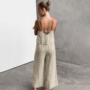 Donna in tuta beige senza maniche, vista posteriore, su sfondo grigio. Moda estiva, abbigliamento casual elegante, tessuto leggero.