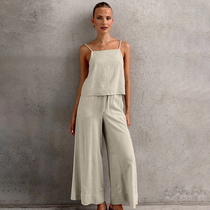 Donna in tuta beige elegante, top senza maniche e pantaloni larghi, posa su sfondo grigio. Moda femminile, abbigliamento estivo casual chic.
