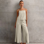 Donna in tuta beige elegante, top senza maniche e pantaloni larghi, posa su sfondo grigio. Moda femminile, abbigliamento estivo casual chic.