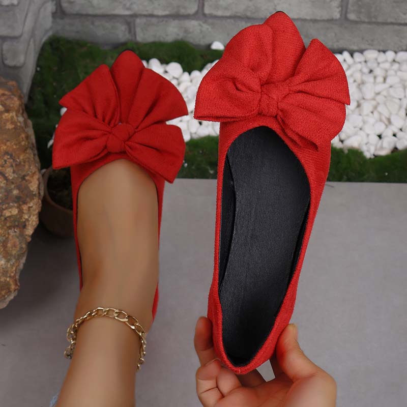Ballerine rosse con fiocco grande, indossate su pavimento grigio. Scarpe eleganti da donna, moda casual, accessorio alla caviglia dorato.