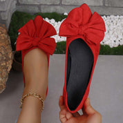 Ballerine rosse con fiocco grande, indossate su pavimento grigio. Scarpe eleganti da donna, moda casual, accessorio alla caviglia dorato.
