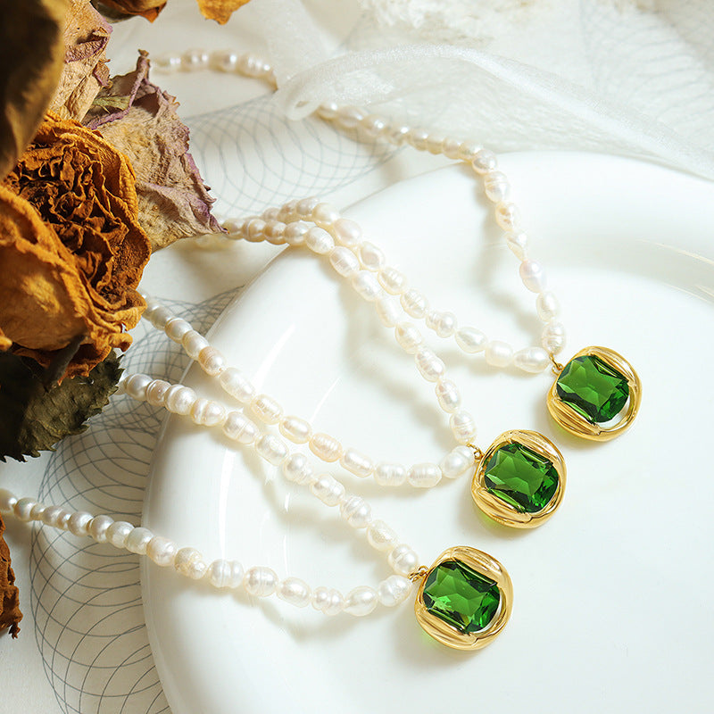 Collana di perle con ciondolo verde smeraldo su piatto bianco, design elegante, gioielli di lusso, accessori moda, regalo perfetto per donna.
