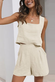 Donna sorridente indossa completo estivo beige in lino, top senza maniche e pantaloncini a vita alta. Moda casual, abbigliamento leggero, look estivo.