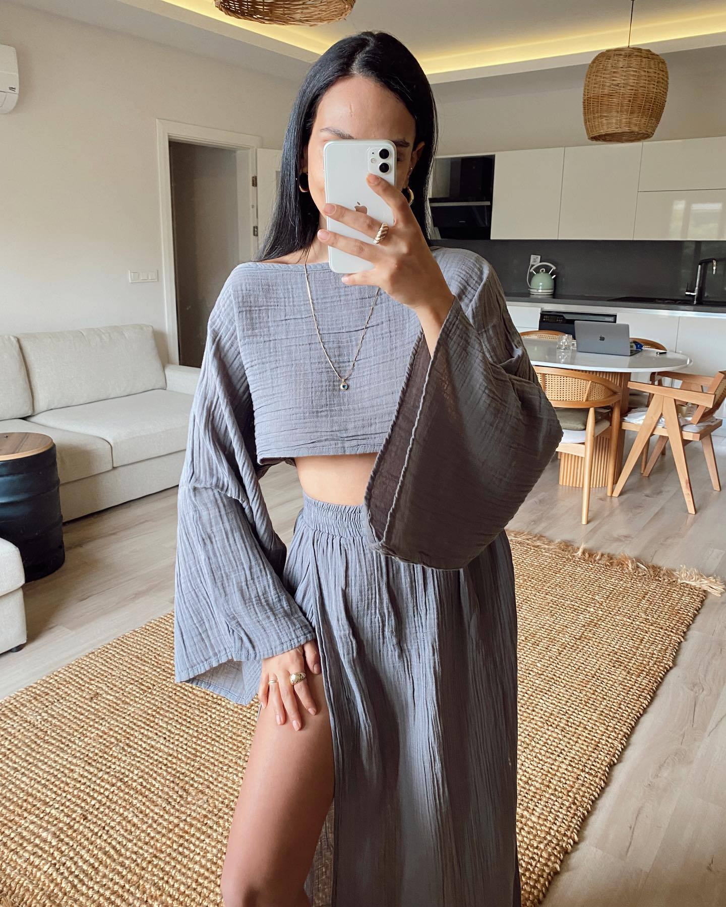 Donna in abito coordinato grigio con top a maniche larghe e gonna lunga con spacco, in soggiorno moderno. Moda femminile, abbigliamento estivo elegante.