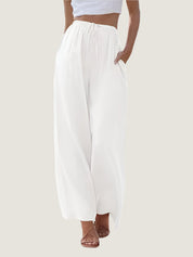 Pantaloni palazzo bianchi da donna, vita alta, tessuto leggero, tasche laterali, abbinati a top corto. Elegante moda estiva casual.