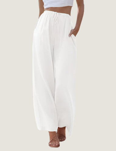 Pantaloni palazzo bianchi da donna, vita alta, tessuto leggero, tasche laterali, abbinati a top corto. Elegante moda estiva casual.