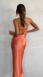Donna in abito lungo arancione satinato, spalle scoperte, tiene un bicchiere di vino. Elegante moda serale, abbigliamento femminile chic.