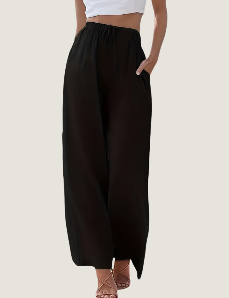 Pantaloni neri larghi da donna, vita alta con coulisse, tasche laterali, abbinati a top bianco corto e sandali. Moda casual estiva.