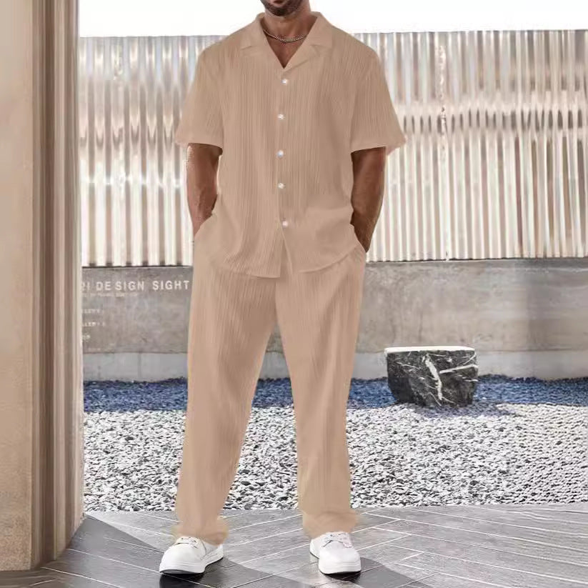 Set coordinato uomo beige, camicia a maniche corte e pantaloni, stile casual estivo, sfondo urbano, moda maschile contemporanea.