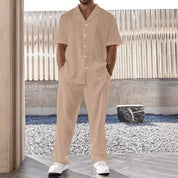 Set coordinato uomo beige, camicia a maniche corte e pantaloni, stile casual estivo, sfondo urbano, moda maschile contemporanea.