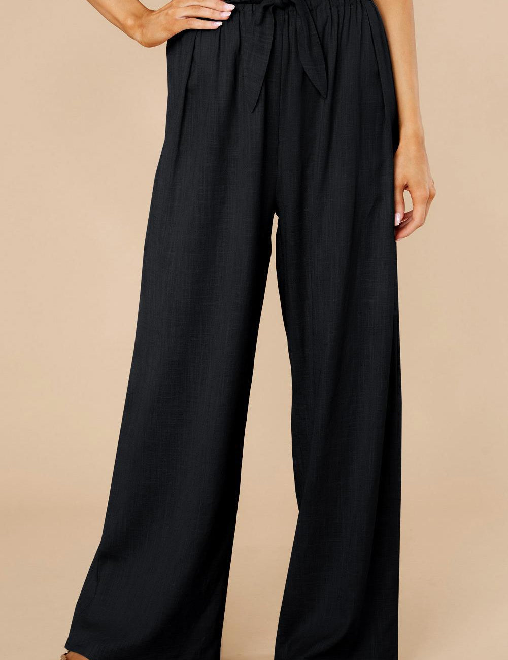 Pantaloni neri a vita alta con cintura, design ampio e pieghe, indossati con sandali. Moda donna elegante, abbigliamento casual chic.
