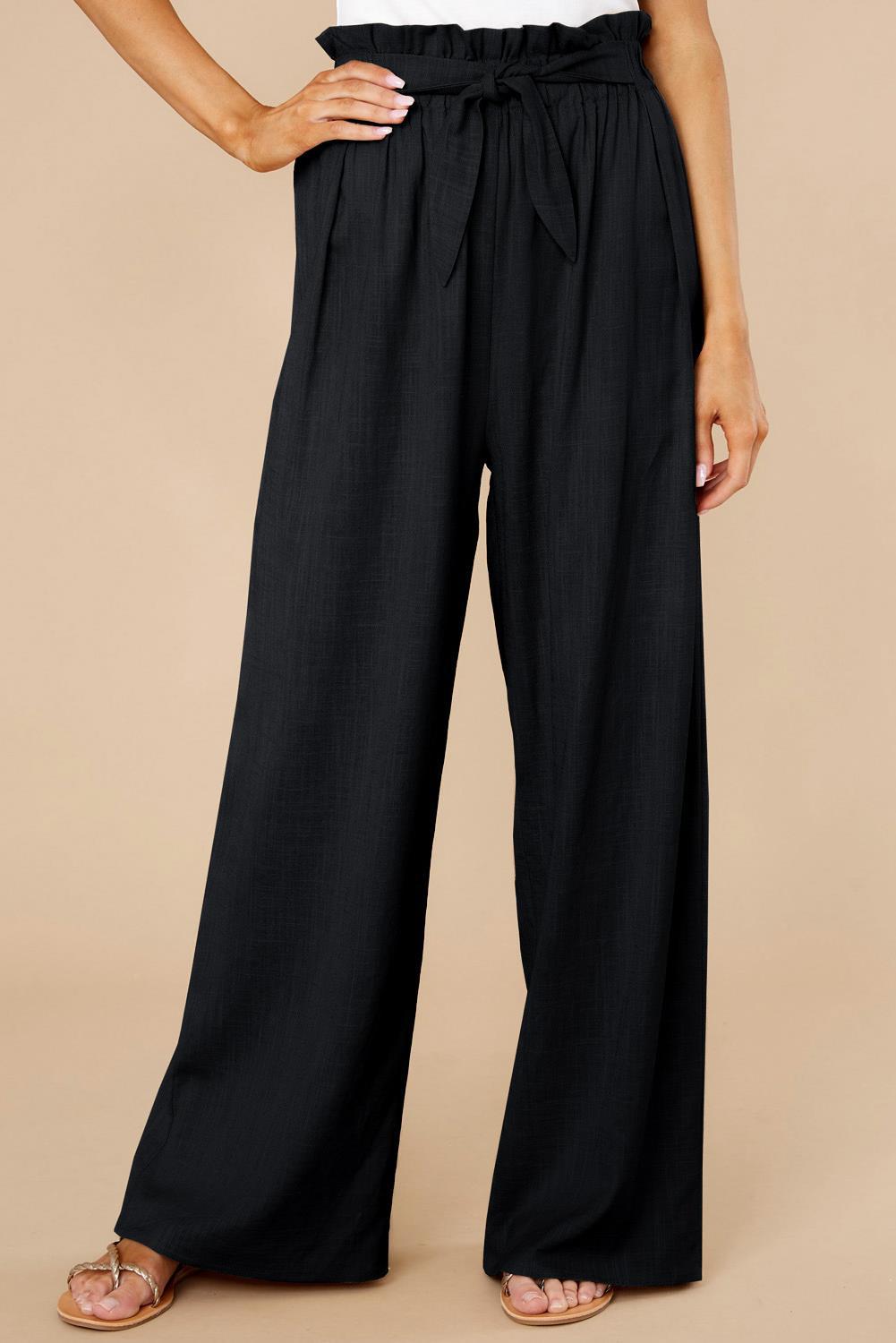 Pantaloni neri a vita alta con cintura, design ampio e pieghe, indossati con sandali. Moda donna elegante, abbigliamento casual chic.