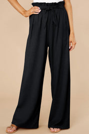 Pantaloni neri a vita alta con cintura, design ampio e pieghe, indossati con sandali. Moda donna elegante, abbigliamento casual chic.