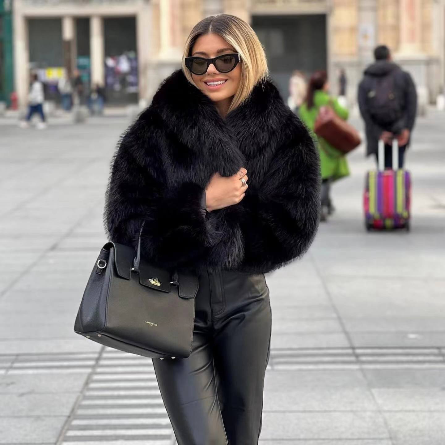 Donna con cappotto di pelliccia nero, occhiali da sole e borsa elegante in piazza cittadina. Moda invernale, stile urbano, abbigliamento di lusso.