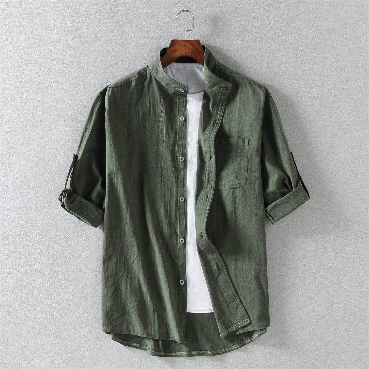 Camicia verde militare da uomo con colletto alla coreana, maniche lunghe arrotolate, tasca frontale, su gruccia. Stile casual, tessuto leggero.