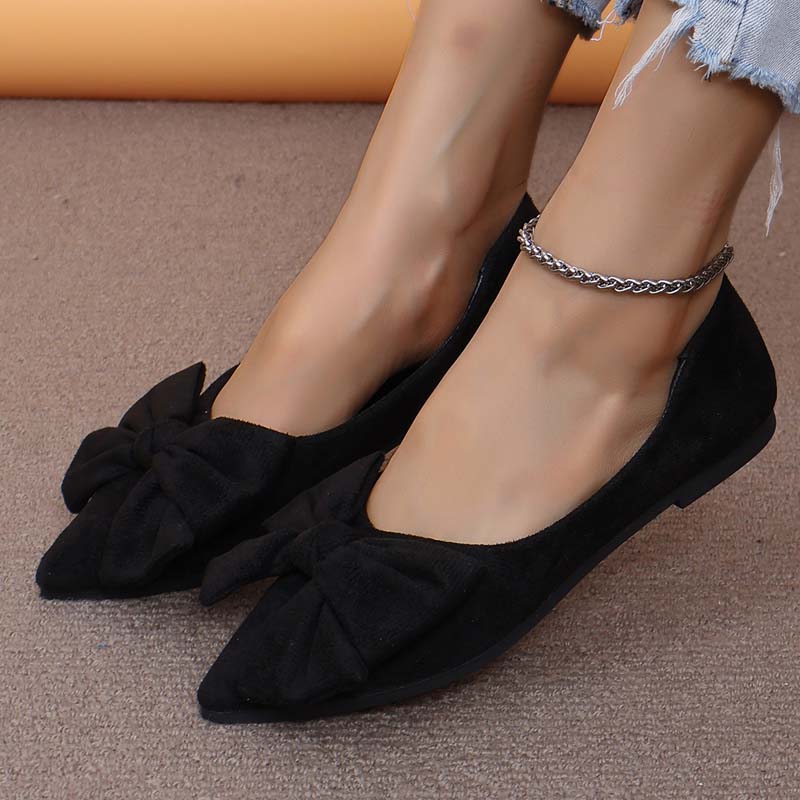 Scarpe ballerine nere da donna con fiocco, indossate su pavimento beige. Design elegante, punta affusolata, perfette per moda casual e formale.
