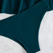 Costume da bagno donna verde scuro, slip bikini a vita alta, tessuto liscio, moda mare estiva, su sfondo marmo bianco.