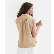 Donna di spalle con camicia beige senza maniche, tessuto leggero, abbinata a pantaloni bianchi. Moda estiva casual, stile minimalista.
