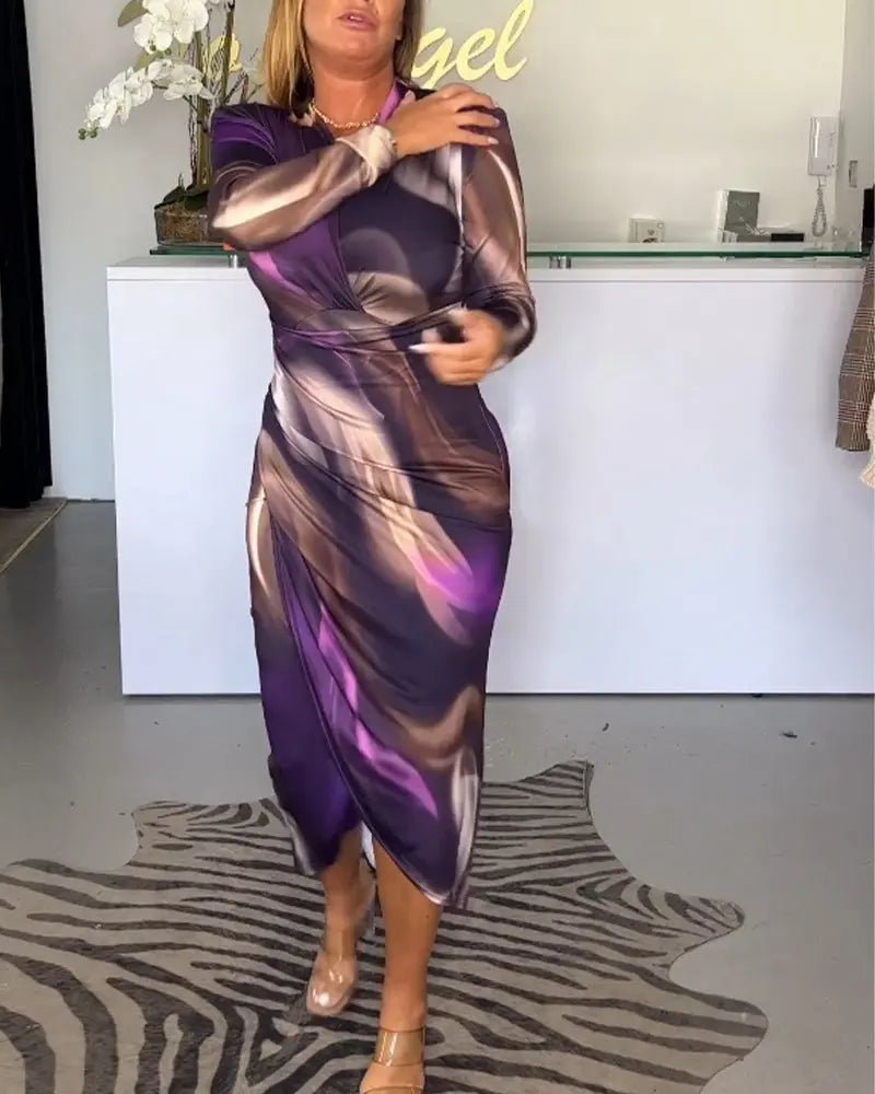 Donna in abito lungo viola con motivi astratti, davanti a un bancone bianco. Indossa sandali trasparenti. Sfondo con decorazioni floreali.