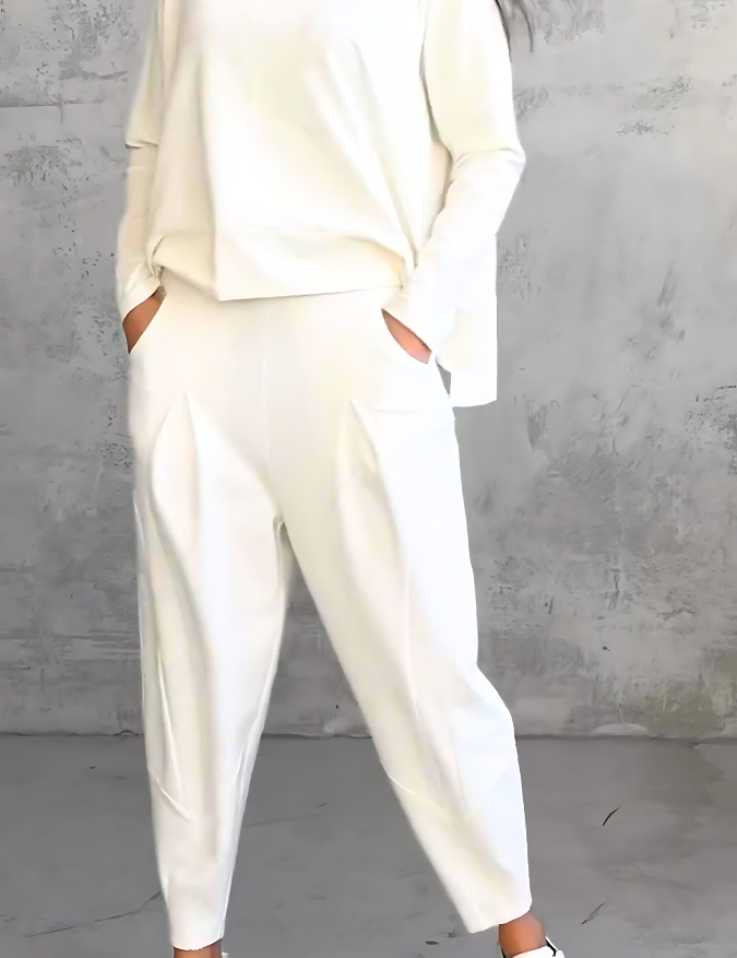 Donna in abbigliamento casual bianco, indossa maglia e pantaloni larghi, con sneakers bianche. Sfondo grigio. Moda minimalista elegante.