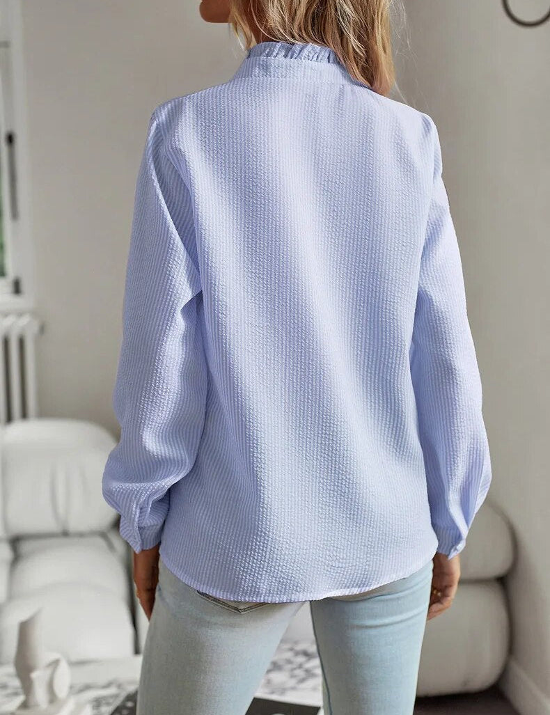 Donna con camicia a maniche lunghe azzurra, tessuto a trama leggera, in un ambiente interno moderno. Moda femminile, abbigliamento casual elegante.